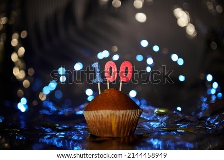Tasty homemade vanilla anniversary cupcake with number 100 one hundred on aluminium foil and blurred bright background in minimalistic style. Digital gift card birthday concept. High quality image