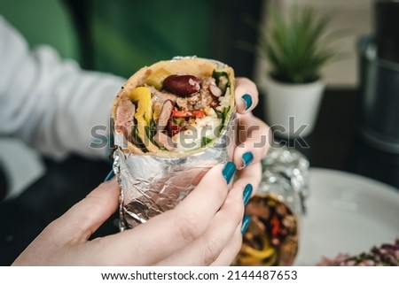 Young woman with red nail polish unpacking the burrito she is holding.