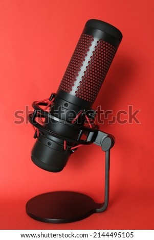 Microphone for podcasts and sound recording. Stands on a red background. Studio condenser microphone in black with red inserts, side view Copy Space. Concept: disinformation, journalism, media