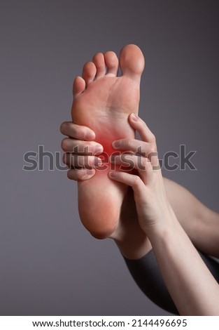 Foot pain in arch. Woman holding leg with red point closeup. Plantar fasciitis, inflammation, injuries, overuse. Health care, orthopedic problems and medicine concept. High quality photo