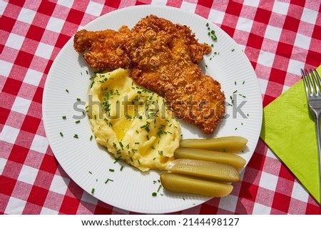 Top view picture on the deep fried chicken escalope or schnitzel with mashed potatoes and pickled cucumbers. Served on white plate with green spring napkin and cutlery. Traditional czech cuisine.