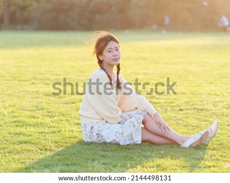 Portrait of elegant Chinese girl in dress sit on meadows enjoy carefree time in forest park in sunny day. Outdoor fashion portrait of glamour young Chinese cheerful stylish woman.