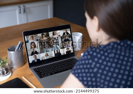 Faces of diverse young business people take part in video conference, laptop screen over female shoulder sit at table involved in group virtual meeting. Modern tech, video call, communication concept Royalty-Free Stock Photo #2144499375