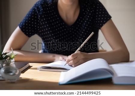 Unknown student girl sit at table with textbook, holds pencil writes essay, prepare for university exams, studying alone indoor, language practice, cram, learns subject, makes chapter overview concept Royalty-Free Stock Photo #2144499425