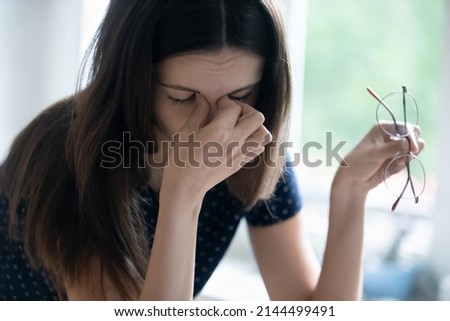 Fatigue, overworking, modern tech usage, blurry vision, dry eyes need drops concept. Close up of young tired woman takes off glasses rubs nose bridge reduces eyestrain feels discomfort and exhaustion Royalty-Free Stock Photo #2144499491