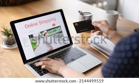 Online shopping, e-commerce retail website usage concept. Laptop monitor view over female, on-line shopping client shoulder, holds credit card purchasing, buy goods, make order, spend money remotely