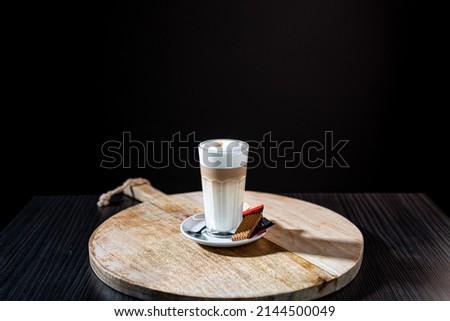 A delicious cup of hot late macchiato with a cookie served on a wooden plate Royalty-Free Stock Photo #2144500049