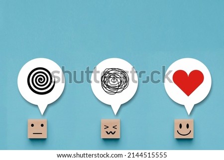 Wooden cube with unhappy face with a tangle of thoughts in its head , wood block with emotion smile happy face and love in thoughts on blue background Royalty-Free Stock Photo #2144515555