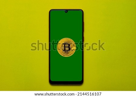 _the bitcoin coin is on a smartphone with a green screen. Light green background. Close-up