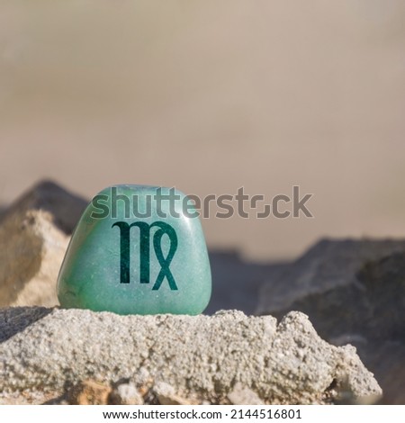 Close-up shot of a stone specifically a teal-colored aventurine engraved with a zodiac sign, in particular the sign of virgo