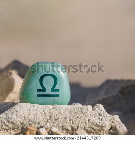 Close-up shot of a stone specifically a teal-colored aventurine engraved with a zodiac sign, in particular the sign of Libra