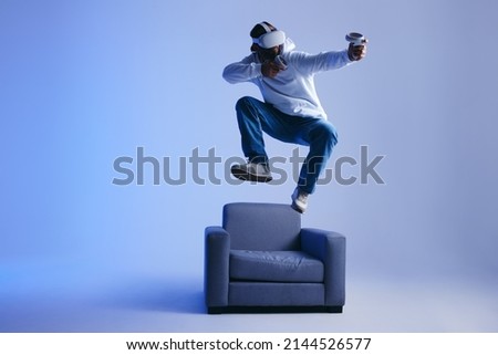 Energetic young man playing an immersive virtual reality game in a studio. Man gaming with virtual reality goggles and controllers. Young man having fun with 3D technology. Royalty-Free Stock Photo #2144526577