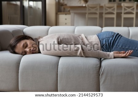 Tired calm young woman resting on spacious sofa in home living room, lying on belly, sleeping at daytime, feeling fatigue after stress, sleepless night. Leisure time, recovery concept Royalty-Free Stock Photo #2144529573
