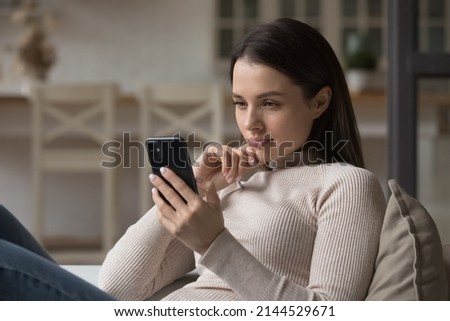 Focused millennial woman using mobile phone at home, reading online content, browsing internet, shopping with application. Gen Z girl texting message on chat on cellphone at home Royalty-Free Stock Photo #2144529671