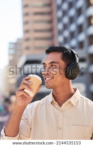 A trendy young businessman listens to music and drinks coffee in the city