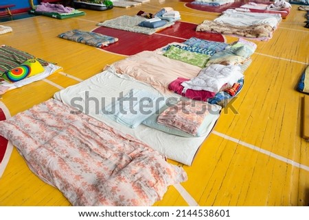 mattresses on the floor in the school gym. temporary housing and accommodation for refugees during the war in Ukraine.  clean beds on the floor for refugees. Royalty-Free Stock Photo #2144538601