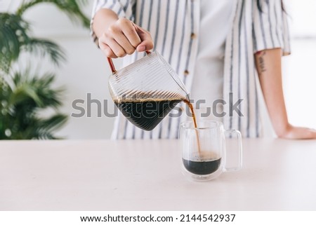 Close up professional barista hand pouring freshly brewed drip coffee in a glass mug. Preparing coffee alternative method.