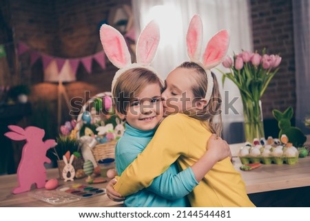 Photo of two peaceful idyllic cute siblings cuddle kiss cheek rabbit ears headband indoors