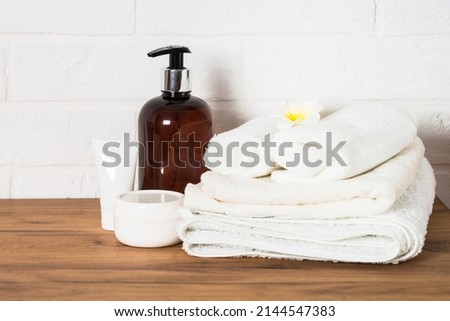 Bottle of soap and stack of towels in white bathroom.