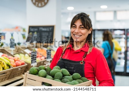 Latin woman working in supermarket holding a box containing fresh avocados Royalty-Free Stock Photo #2144548711