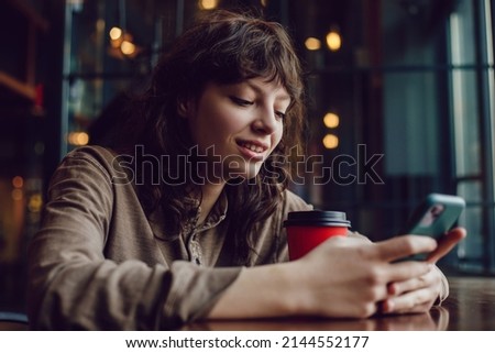 Attractive girl typing messages in the phone while sitting in a cafe.