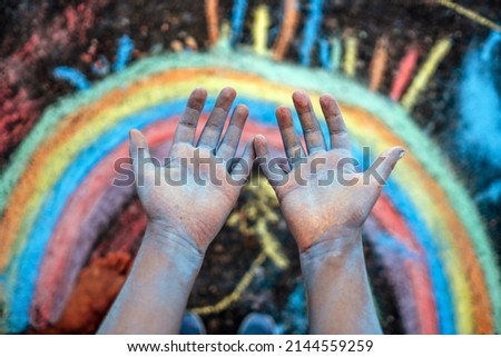 Dirty hands of a girl drawing a rainbow with colored chalks on the playground of the school Royalty-Free Stock Photo #2144559259