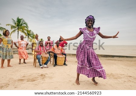 Beautiful black woman dances on a Caribbean beach during a party, wearing a lilac dress.