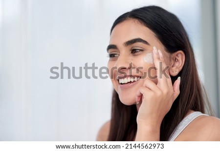 This cream is magic. Shot of a beautiful young woman applying her skincare.