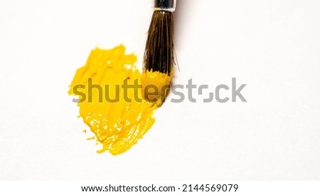 brush draws with yellow paint on a white sheet