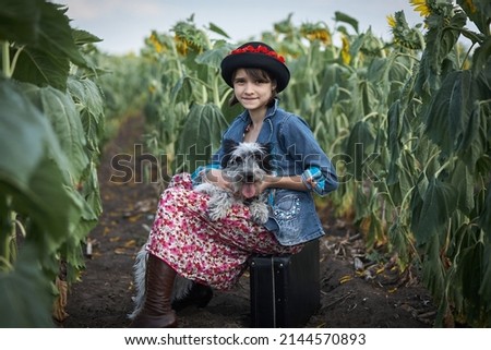 Cute girl with old suitcase and dog in a sunflower field.
