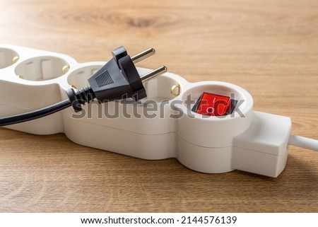 Unplugged electric appliance plug over switched off white power strip on the floor. Power crisis. Increasing the energy costs, heating costs, save electricity concepts. Power outage. Close-up. Royalty-Free Stock Photo #2144576139