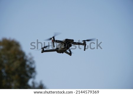an electric white drone with camera flying near to the trees and sky background.