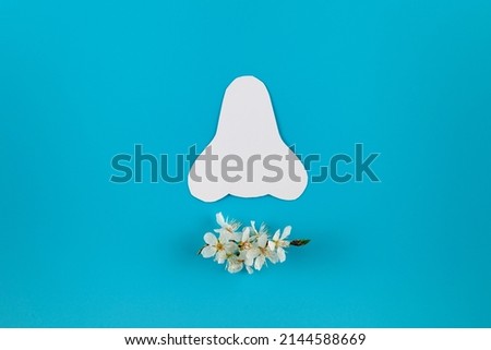 Paper silhouette of a nose and spring flowers on a blue background. Seasonal allergy concept. Flat lay, place for text.
