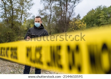 One man police detective or inspector securing crime scene using radio for communication waiting for back up during investigating procedure collecting evidence near the river in day nature copy space Royalty-Free Stock Photo #2144610591