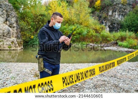 One man police detective or inspector securing crime scene using radio for communication waiting for back up during investigating procedure collecting evidence near the river in day nature copy space Royalty-Free Stock Photo #2144610601
