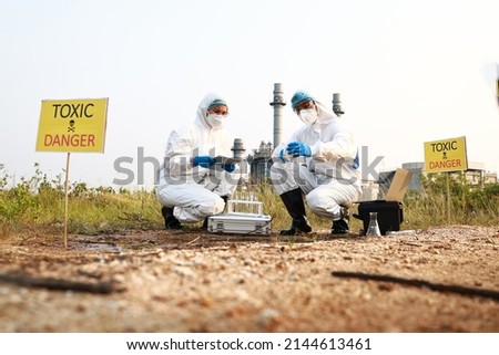 Scientist or Biologist in a protective suit and mask, collects sample of waste water from industrial