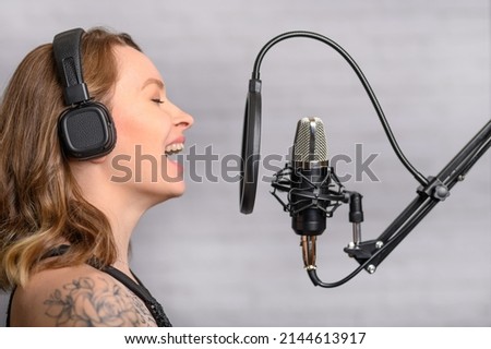 Girl sings into a microphone, in headphones in a studio. Producing and creating songs, music, recording a track. Writing an album