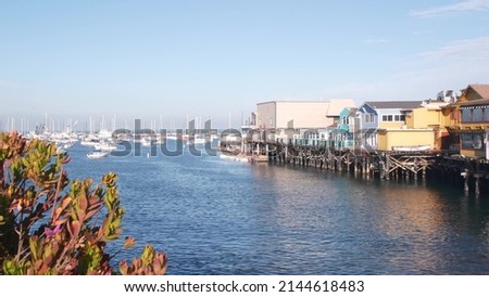 Colorful wooden houses on piles or pillars, ocean bay or harbor, sea water. Old Fisherman's Wharf. Yachts, sail boats in Monterey Marina, California coast USA. Tourist beachfront promenade, flowers. Royalty-Free Stock Photo #2144618483