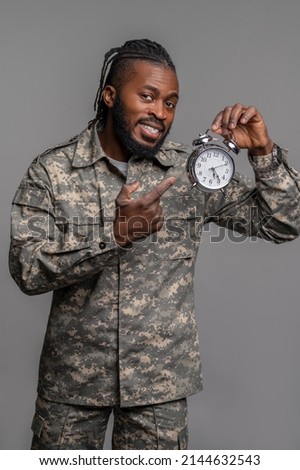 Pleased young military man showing time on his timepiece Royalty-Free Stock Photo #2144632543