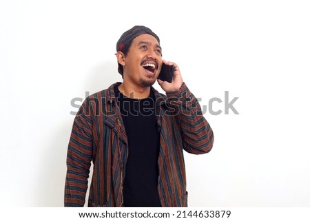 Asian man in javanese traditional costume standing while holding a phone. Isolated on white