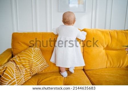child in white clothes on a yellow sofa from the back. High quality photo