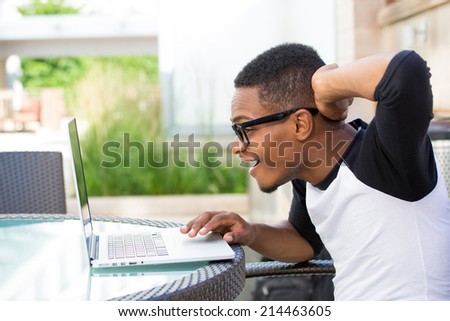 Closeup portrait of nerdy young man, hand on head, amazed in disbelief by what he sees on his personal silver laptop, isolated outdoors outside background. Shocking internet news