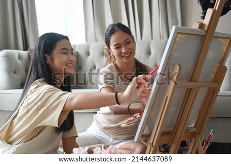 Cheerful asian girl having fun painting with her mother at home.