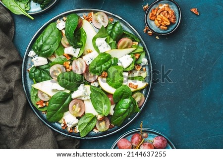 Delicious summer salad with pear, grapes, roquefort cheese, spinach, walnuts on blue table background, top view, negative space