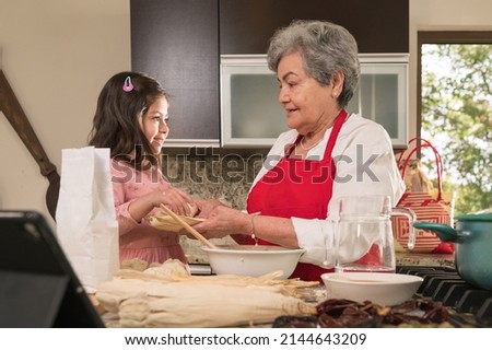 Grandmother teaching her granddaughter to wrap corn tamales in natural dried leaves Royalty-Free Stock Photo #2144643209