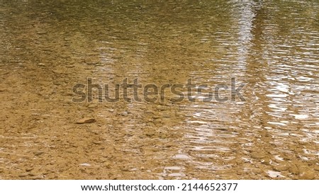 View of the surface of the clear stream where the sand and rocks beneath the water can be clearly seen. 