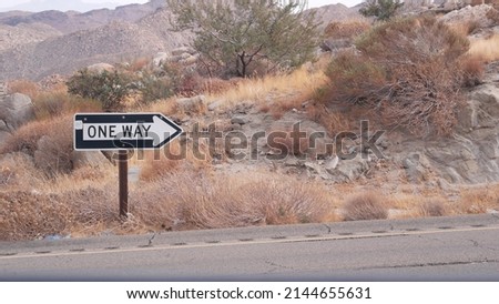 One way road transport sign with arrow on roadside or wayside, highway or freeway in California USA. Road trip in desert valley among mountains and hills with boulders. Western wilderness nature.