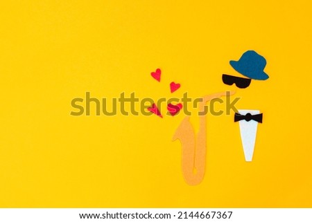 International Jazz Day. Silhouette of a musician with a saxophone, which hearts and flew out on a yellow background, cutted out of felt. Copy space. Flat lay.