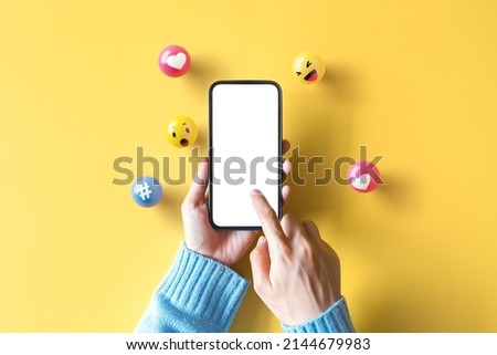 Hand of woman holding blank mobile phone with love, like, comment, hashtag button on yellow background. Social media marketing concept