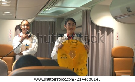 Asian stewardess safety explaining passengers prior to flight take off in airplane, air hostess uniform safety demonstration presenting pre-flight safety instructions life vest in emergency situation Royalty-Free Stock Photo #2144680143